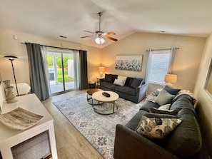 Spacious Living room with large smart TV, ceiling fan, new furniture, and access to covered back patio.