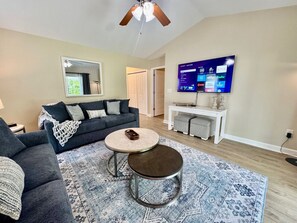 Spacious Living room with large smart TV, ceiling fan, new furniture, and access to covered back patio.