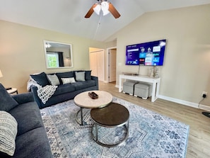 Spacious Living room with large smart TV, ceiling fan, new furniture, and access to covered back patio.