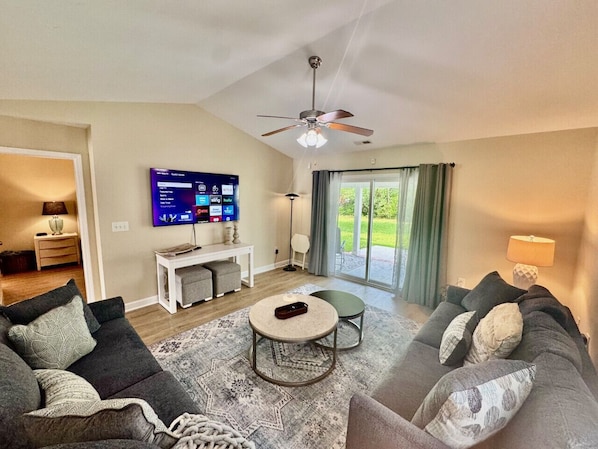 Spacious Living room with large smart TV, ceiling fan, new furniture, and access to covered back patio.