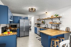 This stylish kitchen features bold blue cabinets, butcher block countertops, and open shelving—perfect for everything from family meals to morning coffee rituals.