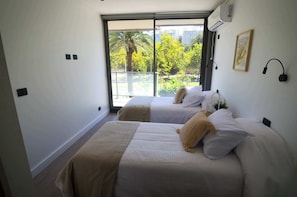 Bright and cozy bedroom with twin beds, offering a serene view of lush greenery and a palm tree, perfect for a relaxing stay.