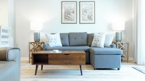 living room - Relax in the cozy living room, featuring a comfortable sofa perfect for unwinding after a day at the beach. Two stylish end tables with soft-glow lamps create a warm, inviting ambiance for evening lounging or reading. Step through the sliding doors to your private back deck—ideal for morning coffee or sunset cocktails with a gentle ocean breeze.