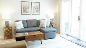 living room - Relax in the cozy living room, featuring a comfortable sofa perfect for unwinding after a day at the beach. Two stylish end tables with soft-glow lamps create a warm, inviting ambiance for evening lounging or reading. Step through the sliding doors to your private back deck—ideal for morning coffee or sunset cocktails with a gentle ocean breeze.