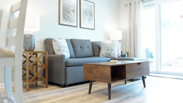 living room - Relax in the cozy living room, featuring a comfortable sofa perfect for unwinding after a day at the beach. Two stylish end tables with soft-glow lamps create a warm, inviting ambiance for evening lounging or reading. Step through the sliding doors to your private back deck—ideal for morning coffee or sunset cocktails with a gentle ocean breeze.
