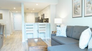 Relax in the cozy living room, featuring a comfortable sofa perfect for unwinding after a day at the beach. Two stylish end tables with soft-glow lamps create a warm, inviting ambiance for evening lounging or reading. Step through the sliding doors to your private back deck—ideal for morning coffee or sunset cocktails with a gentle ocean breeze.