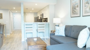 Relax in the cozy living room, featuring a comfortable sofa perfect for unwinding after a day at the beach. Two stylish end tables with soft-glow lamps create a warm, inviting ambiance for evening lounging or reading. Step through the sliding doors to your private back deck—ideal for morning coffee or sunset cocktails with a gentle ocean breeze.