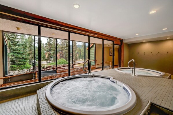 A tranquil spa area with large windows, featuring a relaxing hot tub and serene forest views.