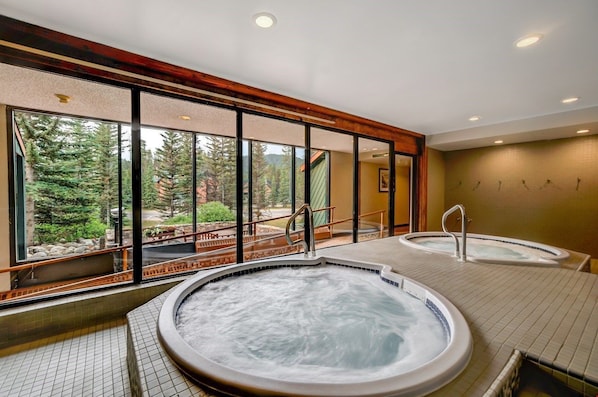 A tranquil spa area with large windows, featuring a relaxing hot tub and serene forest views.
