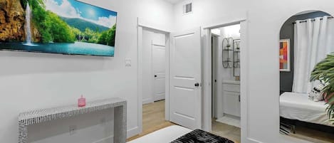 The bedroom includes a 55" smart TV and a stylish console, providing both entertainment and storage in one sleek setup. The bedroom also features a full-length mirror, adding functionality and a touch of elegance to the space.