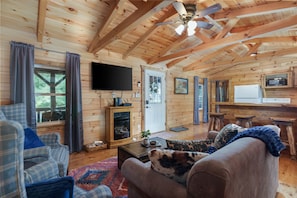 Cozy up in this charming cabin living room 🛋️🔥. Featuring warm wood finishes, a comfy sofa, and an electric fireplace under vaulted ceilings—perfect for movie nights or simply unwinding in rustic comfort 🌲📺