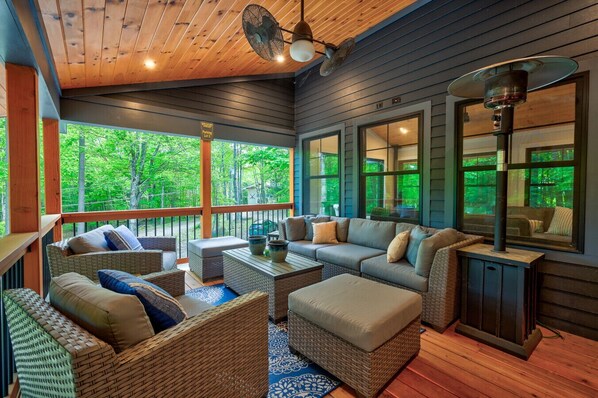 Covered porch with cozy seating, rotating ceiling fans, and peaceful views of the surrounding woods.