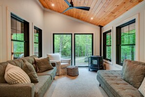 Cozy reading room with forest views, plush seating, ceiling fan, and a wood-burning pellet stove.