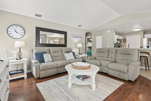 Spacious open-concept living room with cozy seating, flowing into the dining area and kitchen, with views of the patio and backyard oasis.