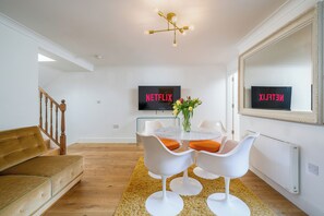 The bright and airy living and dining area features a chic marble-top table with retro-inspired white chairs, complemented by cozy orange seat cushions.
The inviting mustard-colored sofa adds warmth, offering the perfect spot to unwind.