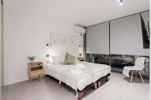 Relax in this serene, modern bedroom with cozy bedding, ambient lighting, and a wall-mounted TV for ultimate comfort.