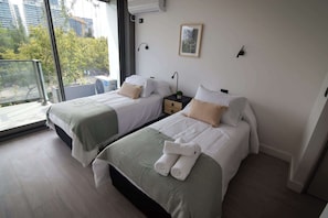 Bright and airy bedroom with two cozy beds, modern decor, and a lovely view, perfect for a relaxing stay.