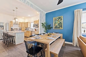 This wood dining set comfortably seats 10 surrounded by modern chairs and a bench. The space is illuminated by soft lighting creating a warm and inviting atmosphere with close proximity to the kitchen, making entertaining easier.
