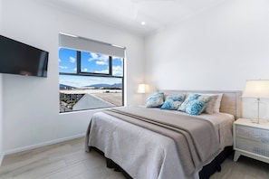 The spacious primary bedroom is appointed with a king-size bed and a TV while offering sweeping views overlooking the city and mountain ranges.