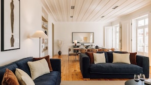 Spacious living room with two navy sofas, wooden floors, natural light, elegant decor, and cozy, inviting atmosphere. 
#AndoLiving
#CozyLiving 
#InteriorDesign 
#ModernHome