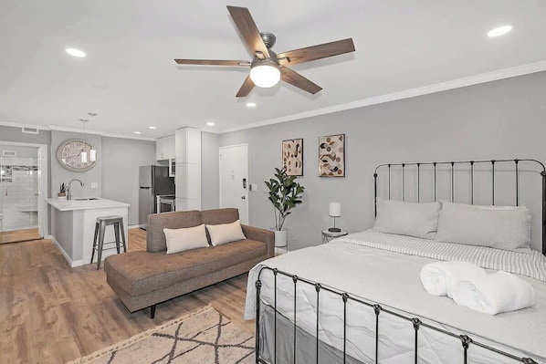 A very cute studio apartment with a couch and a queen iron wrought frame bed.