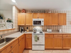 Discover a bright and inviting full kitchen featuring wooden cabinetry, modern appliances, and a cozy coastal charm perfect for culinary adventures in the Sea Colony West townhome.