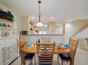 The open-concept dining area showcases coastal-inspired decor, complemented by a well-lit ambiance and a view into the full kitchen, ideal for gatherings.