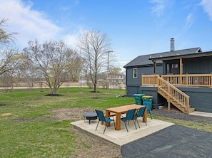 Back view of home and outdoor dining table and fire pit.