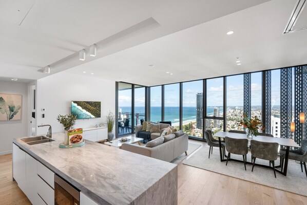 Open-plan luxury kitchen and living area bathed in natural light from soaring 2.85m floor-to-ceiling glass windows.