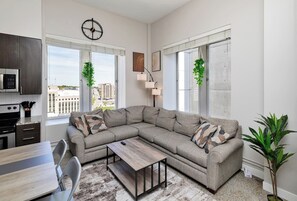 Living area with sectional couch, roku smart TV and large windows with downtown skyline view.