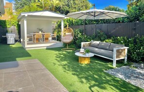 Enjoy the lush backyard oasis with a couch, umbrella, and swing chair.