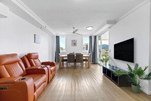 Unwind in the open-plan living area with leather recliners, natural light, and a wall-mounted TV—perfect for a relaxed evening in.