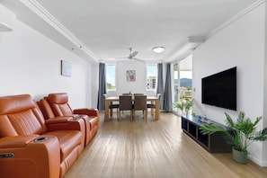 Unwind in the open-plan living area with leather recliners, natural light, and a wall-mounted TV—perfect for a relaxed evening in.