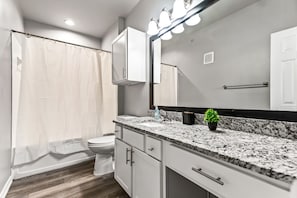 This bright and welcoming bathroom invites you to freshen up in comfort. Enjoy the forest-inspired shower curtain that adds a calming touch to your routine, complemented by the cozy rug underfoot and sparkling clean fixtures.