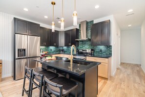 Unit 2: Sleek kitchen with black cabinetry, stainless steel appliances, and a spacious island for dining or gathering. (2nd Floor)