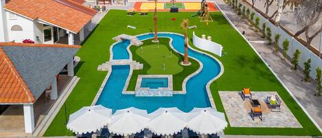 Take in the breathtaking aerial view of this expansive backyard, featuring a sparkling pool, winding lazy river, sport court, putting green, and plenty of lounge chairs—perfect for entertaining, relaxing, and making unforgettable memories.