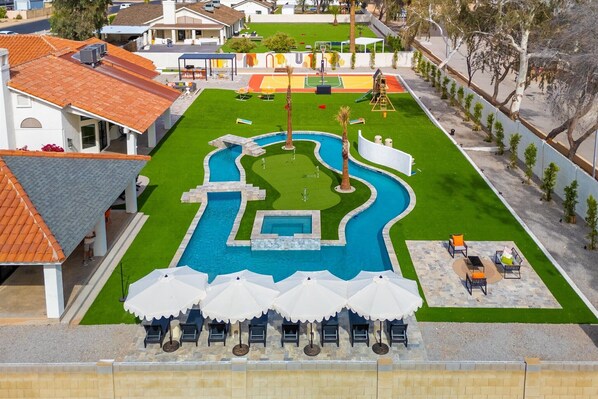 Take in the breathtaking aerial view of this expansive backyard, featuring a sparkling pool, winding lazy river, sport court, putting green, and plenty of lounge chairs—perfect for entertaining, relaxing, and making unforgettable memories.