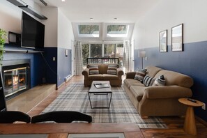Spacious living room with plenty of natural light, comfy couches, large smart TV and fireplace