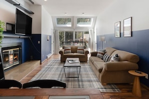 Spacious living room with plenty of natural light, comfy couches, large smart TV and fireplace