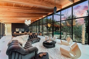 Experience serene luxury in our modern retreat. This open-concept space features floor-to-ceiling windows with breathtaking views, a plush velvet sofa, and contemporary furnishings.