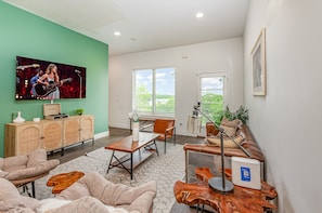Welcoming living area with a vibrant green accent wall, large Smart TV, and plush seating arranged to take in the serene outside views.
