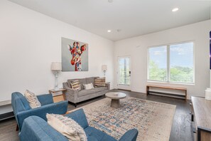 Unit 2: Living room boasts an open-concept layout with comfy seating, a patterned rug, and large windows that bathe the room in natural light.