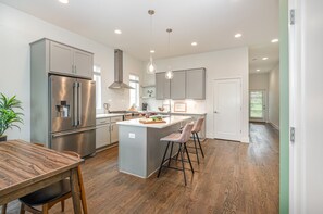 Unit 1: Bright open-concept kitchen featuring a quartz-topped island with bar seating, stainless steel appliances, and abundant natural light streaming through the windows.