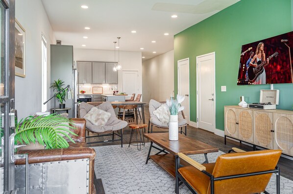 Unit 1: Welcoming living area with a vibrant green accent wall, large Smart TV, and plush seating arranged to take in the serene outside views.