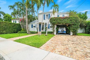 Beautiful two-story home is nestled amongst lush greenery, with a unique covered parking area adding to its character.
