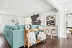 Bright and open living space features a comfortable teal sectional, a wooden console table, and a view into the modern kitchen.
