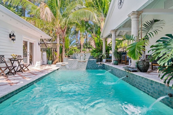 Beautiful pool area is surrounded by lush tropical greenery and offers various seating options for enjoying the tranquil setting.