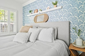Serene bedroom boasts a comfortable bed with soft white linens and a unique shelf against a patterned accent wall.