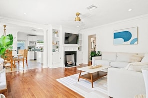 Bright and open living area boasts hardwood floors, comfortable white sofas, a fireplace, and a mounted TV for relaxation.