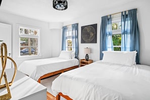 Bright and airy bedroom offers two comfortable beds with white linens and blue accents, along with a mounted television.